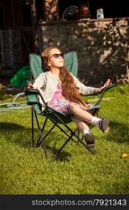 Beautiful young girl relaxing in armchair on grass at sunny day