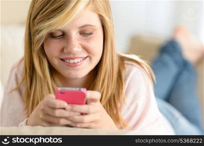 Beautiful young girl texting on her cellphone lying on sofa