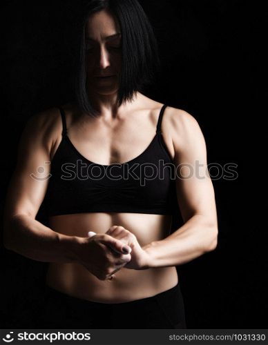 beautiful young girl with a sports figure dressed in a black top claps in her hands with white magnesia, preparing before exercise, low key