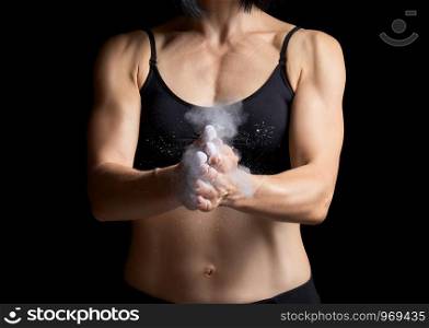 beautiful young girl with a sports figure dressed in a black top claps in her hands with white magnesia, preparing before exercise, loy key