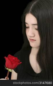 Beautiful young girl with long black hair and pale complexion looking at red rose. Shot in studio over black.
