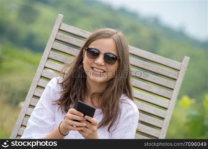 beautiful young girl with sunglasses is using a smartphone