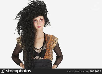 Beautiful young Goth woman with teased hair looking away over gray background