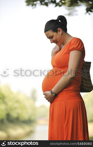 beautiful young happy pregnant woman outdoor in bright nature in orange dress