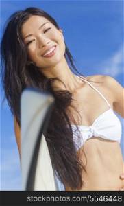 Beautiful young Hawaiian Asian woman surfer girl in bikini with surfboard standing in the surf on a beach