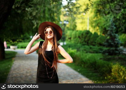 Beautiful young hipster woman outdoors, wearing black dress, hat and vintage sunglasses