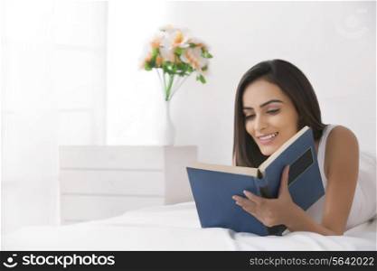 Beautiful young Indian woman reading book in bed