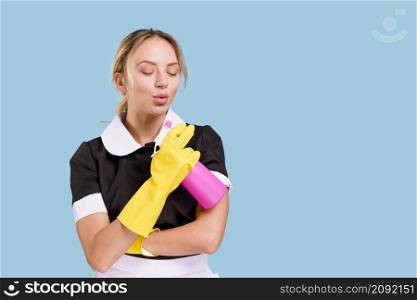 beautiful young janitor holding spray bottle blowing with eyes closed blue background