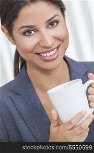 Beautiful young Latina Hispanic woman businesswoman with perfect teeth, smiling &amp; relaxing in her office drinking a cup of coffee or tea