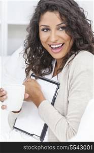 Beautiful young Latina Hispanic woman laughing, relaxing, using a tablet computer and drinking tea or coffee