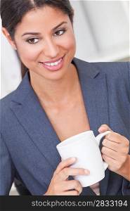 Beautiful young Latina Hispanic woman or business woman smiling, relaxing and drinking a cup of tea or coffee in her office