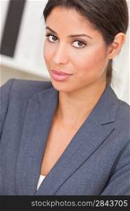 Beautiful young Latina Hispanic woman or businesswoman in smart business suit sitting at a desk in an office