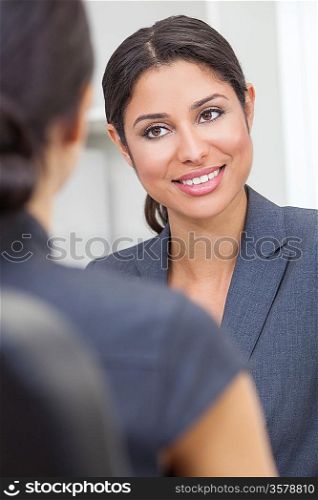 Beautiful young Latina Hispanic woman or businesswoman in smart business suit sitting at a desk in an office having a meeting with colleague
