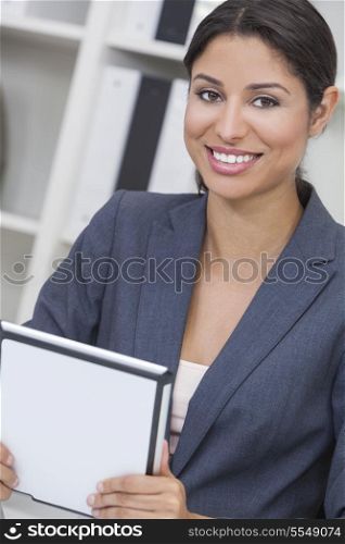 Beautiful young Latina Hispanic woman or businesswoman in smart business suit sitting at a desk in an office using a tablet computer