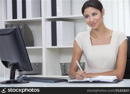 Beautiful young Latina Hispanic woman or businesswoman sitting at a desk in an office writing in her diary