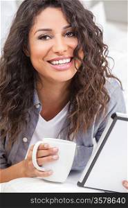 Beautiful young Latina Hispanic woman smiling, relaxing and drinking a cup of coffee or tea using tablet computer