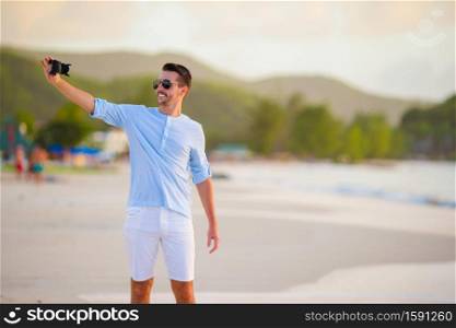 Beautiful young man taking a photo herself on tropical beach. Beautiful young man taking a self photo herself on tropical beach