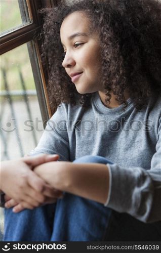 Beautiful young mixed race African American girl sitting smiling and looking out of a rain covered window