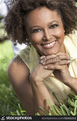 Beautiful young mixed race black African American woman with perfect teeth smiling and relaxing laying down on grass outside in summer sunshine