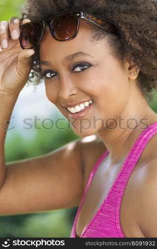 Beautiful young mixed race black African American woman with perfect teeth smiling and wearing lifting her sunglasses outside in summer sunshine