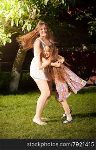 Beautiful young mother and daughter dancing on grass at yard