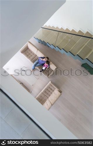 Beautiful young mother and her cute little daughter are using a tablet and smiling, sitting on sofa at home top view