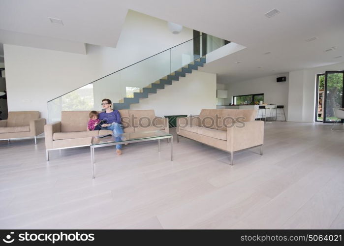 Beautiful young mother and her cute little daughter are using a tablet and smiling, sitting on sofa at home