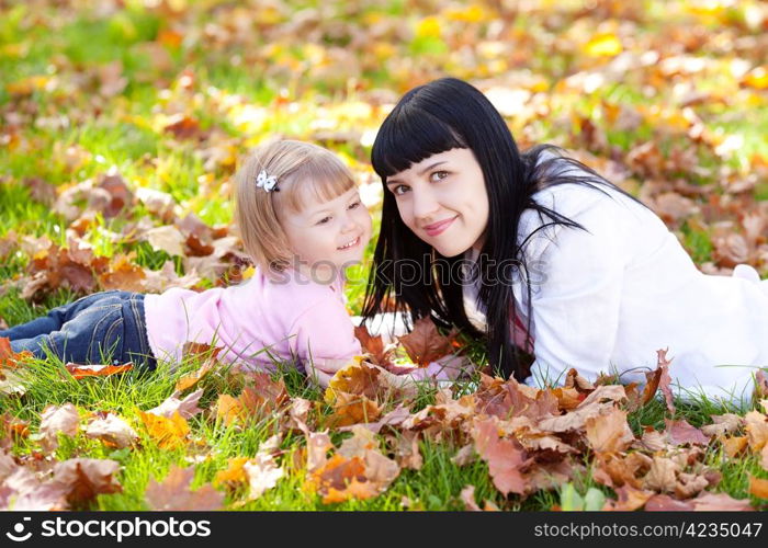 beautiful young mother and her daughter lying on the autumn leaves