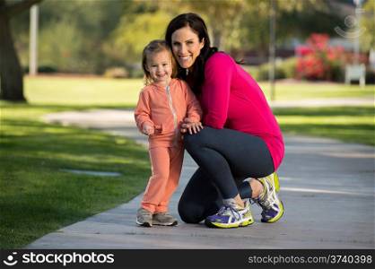 Beautiful young mother and her daughter playing in the neighborhood. They are on a sidewalk in a grassy greenbelt.