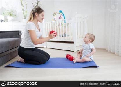 Beautiful young mother doing fitness and giving dumbbells to her baby. Concept of family sport