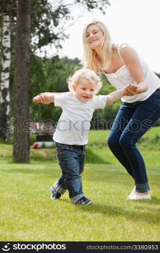 Beautiful young mother helping her adorable little boy to walk