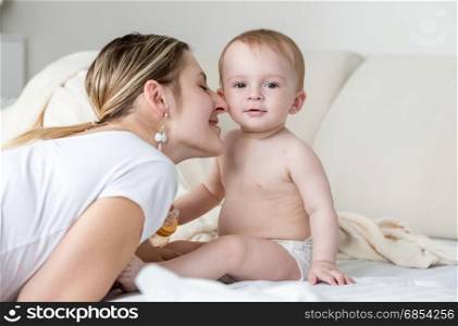 Beautiful young mother kissing baby boy in cheek on bed