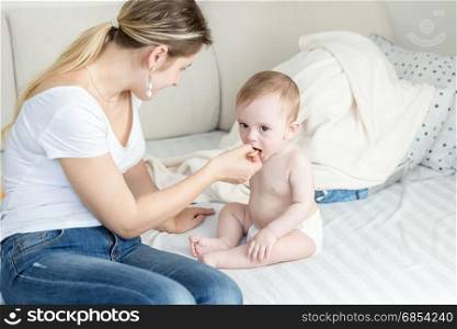 Beautiful young mother sitting with her baby on sofa and giving him a cookie