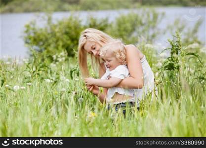 Beautiful young mother spending her time with her little son in grass