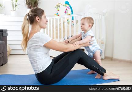 Beautiful young mother stretching on fitness mat with her baby boy