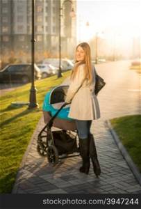 Beautiful young mother walking with baby stroller on sunny street