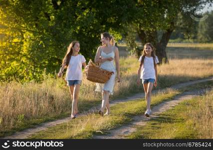 Beautiful young mother walking with her daughter in meadow at sunset