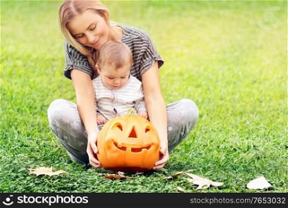 Beautiful young mother with adorable little child, playing with carved pumpkin, enjoying traditional autumn holiday, happy Halloween celebration