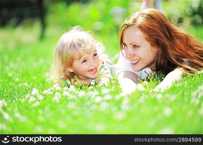 Beautiful young mother with her daughter lie on grass . summer.