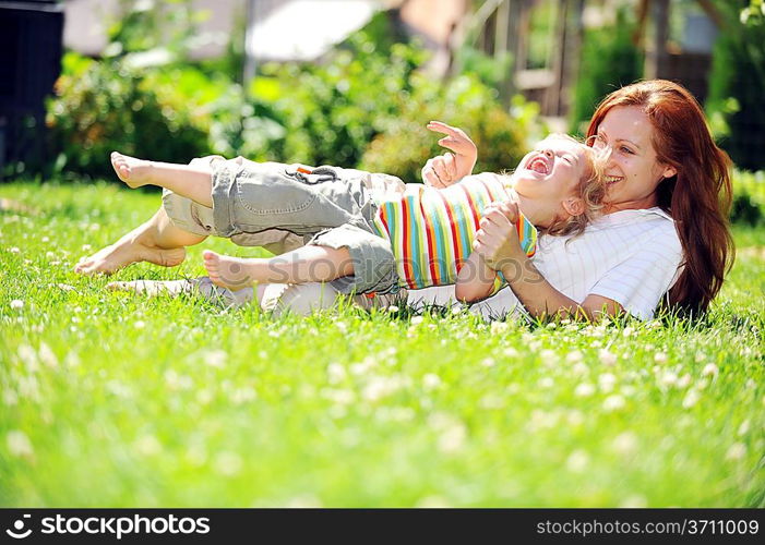 Beautiful young mother with her daughter playing on grass . summer.