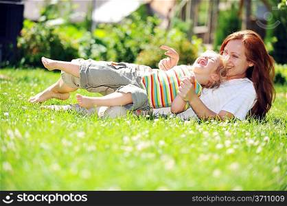 Beautiful young mother with her daughter playing on grass . summer.