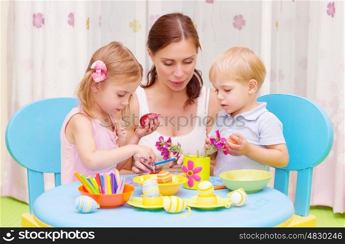 Beautiful young mother with two sweet kids decorated traditional Easter eggs with colorful paint, happy family concept&#xA;