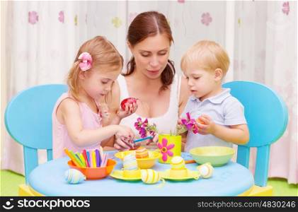 Beautiful young mother with two sweet kids decorated traditional Easter eggs with colorful paint, happy family concept&#xA;