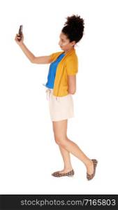 Beautiful young multi-racial woman standing in shorts and a yellow sweater in profile looking at cellphone isolated for white background