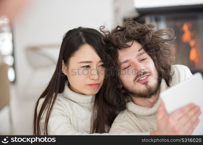 beautiful young multiethnic couple using tablet computer in front of fireplace on cold winter day at home