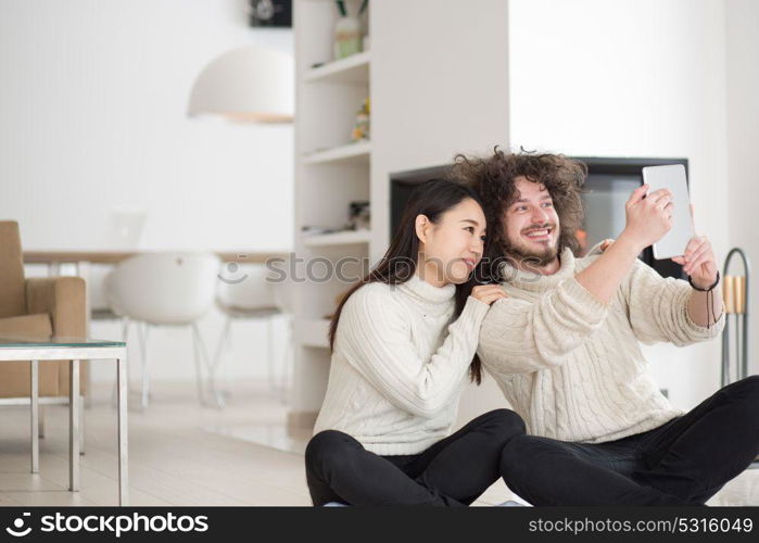 beautiful young multiethnic couple using tablet computer in front of fireplace on cold winter day at home