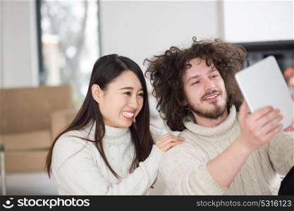 beautiful young multiethnic couple using tablet computer in front of fireplace on cold winter day at home