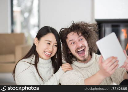 beautiful young multiethnic couple using tablet computer in front of fireplace on cold winter day at home