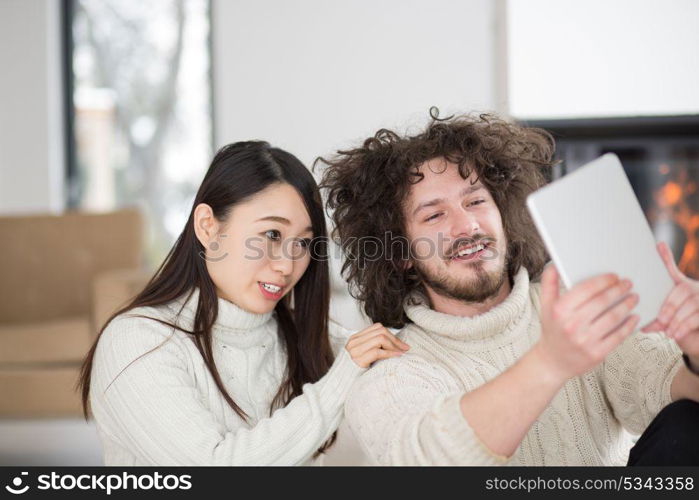 beautiful young multiethnic couple using tablet computer in front of fireplace on cold winter day at home