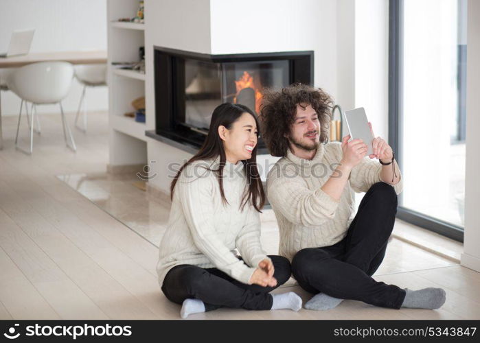 beautiful young multiethnic couple using tablet computer in front of fireplace on cold winter day at home